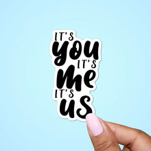 Load image into Gallery viewer, This sticker is a sticker made with a quote from a tv show. The quote reads its&#39; you it&#39;s me, its us and emphasize the words you me and us.  All the words are written in black and  a hand is holding the sticker from the right bottom corner. 
