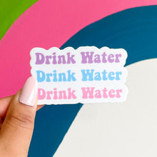 Load image into Gallery viewer, drink water reminder sticker being held by a woman&#39;s hand against a strake of colors painted on a wall
