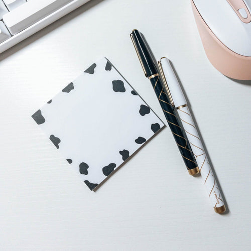 Black and white cow print patterned note pad / memo pad on the desk next to a couple of pens and a mouse.